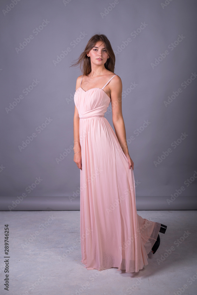 Young girl in a pink dress posing on a gray background.