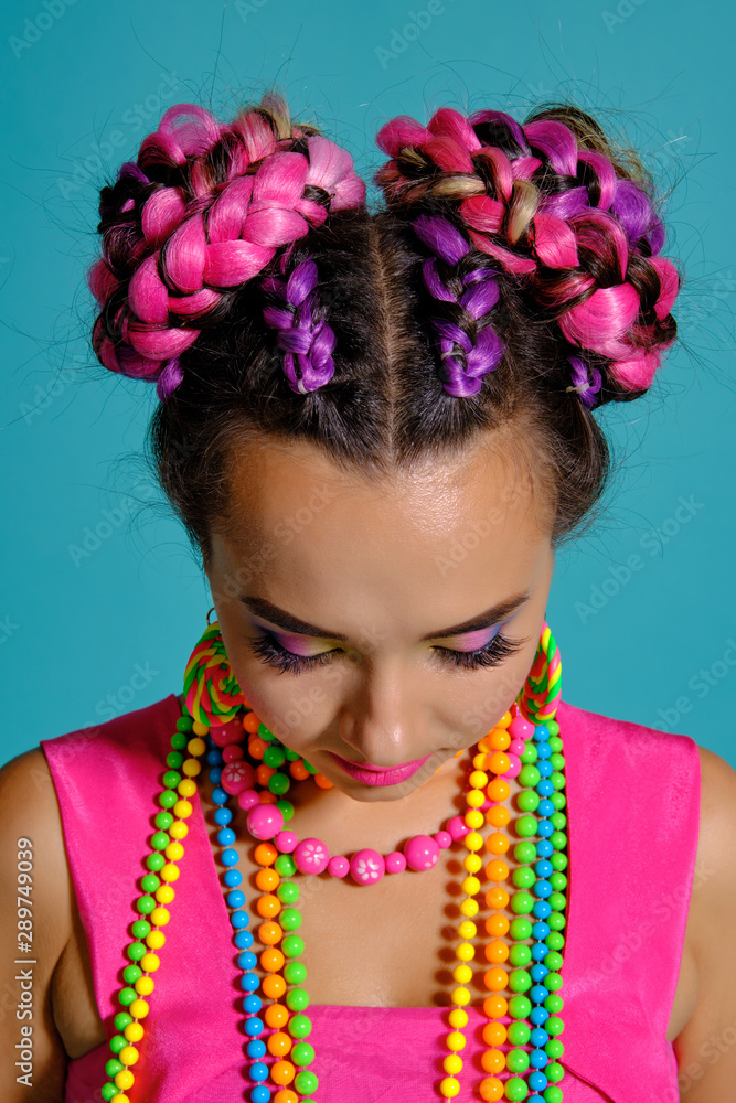 Lovely girl with a multi-colored braids hairstyle and bright make-up, posing in studio against a blue background. Lovely girl with a multi-colored braids hairstyle and bright make-up, posing in studio against a blue background.