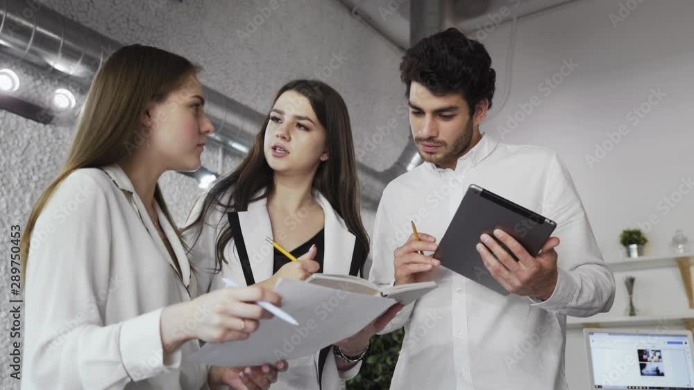 Group of Young Smart Professionals Talking, Holding in Hands Paper and See Them, on Background of modern loft office Group of Young Smart Professionals Talking, Holding in Hands Paper and See Them, on Background of modern loft office
