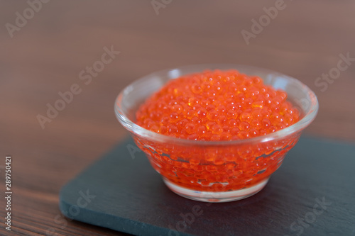 Red caviar in the glass jar on the dark brown wooden background