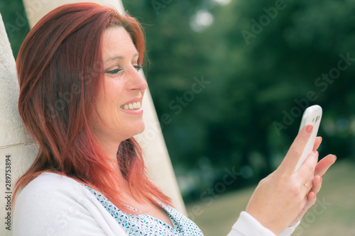 Pretty smiling redhead woman sending messages on her cell phone