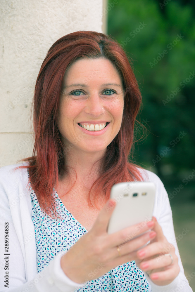 Pretty smiling redhead woman sending messages on her cell phone Pretty smiling redhead woman sending messages on her cell phone