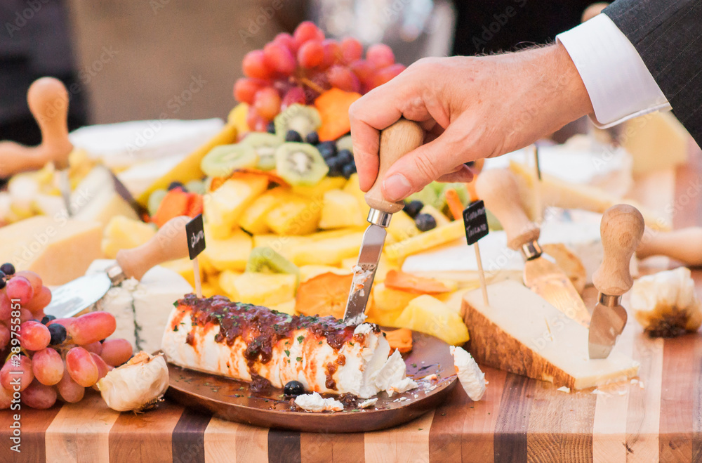 fancy appetizer plate at wedding, cheese platter with kiwi slices, grapes, berries, pineapple, goat cheese, brie, crackers, on a wooden cutting board, event appetizers, variety of hard cheeses