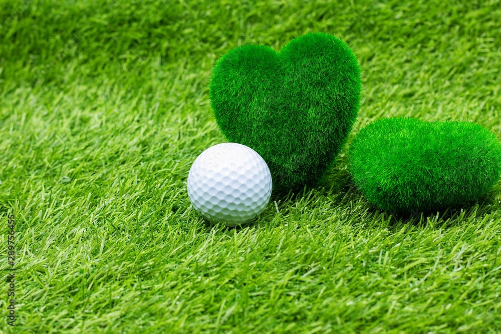Golf ball and green grass heart shape are on green grass. Golf ball and green grass heart shape are on green grass.