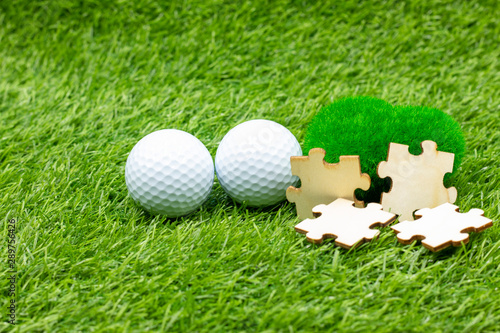 Golf ball and jigsaw are on green grass