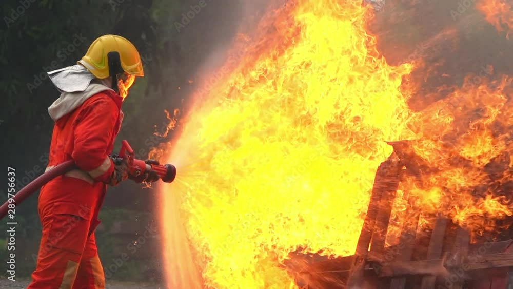 HD Slow motion medium shot of firefighter in fire suit on safety rescue duty using water extinguisher from a hose extinguishing crackle fire flames inside burning premises. Fireman fighting a fire. HD Slow motion medium shot of firefighter in fire suit on safety rescue duty using water extinguisher from a hose extinguishing crackle fire flames inside burning premises. Fireman fighting a fire.