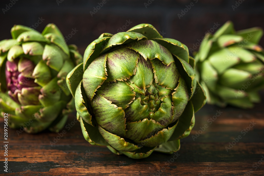Fototapeta premium Fresh raw organically grown artichoke flower buds on wooden table