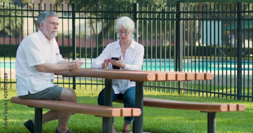 A mature couple sitting at a picnic table disengaged due to the typical addictive behavior of dependency on smart phone use. A mature couple sitting at a picnic table disengaged due to the typical addictive behavior of dependency on smart phone use.
