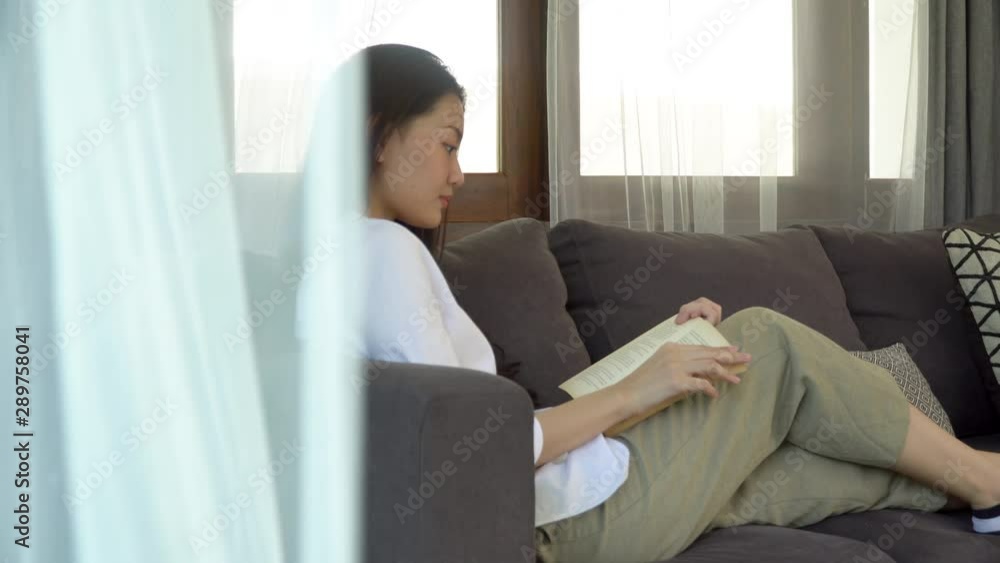4K Medium shot zoom in of Beautiful young asian woman relaxing lying down on sofa in living room and reading a book. Pretty teenage girl resting on sofa and enjoying to read at home in weekend alone 4K Medium shot zoom in of Beautiful young asian woman relaxing lying down on sofa in living room and reading a book. Pretty teenage girl resting on sofa and enjoying to read at home in weekend alone