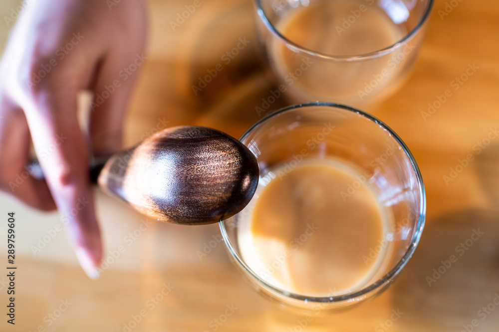Flat top closeup view of two glasses with fermented Japanese traditional rice drink of amazake on kitchen wooden table with woman hand holding wood ladle spoon in Japan Flat top closeup view of two glasses with fermented Japanese traditional rice drink of amazake on kitchen wooden table with woman hand holding wood ladle spoon in Japan