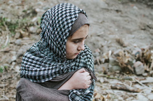a refugee child in the war, a Muslim girl with a dirty face on the ruins, the concept of peace and war, the child is crying and waiting for help.