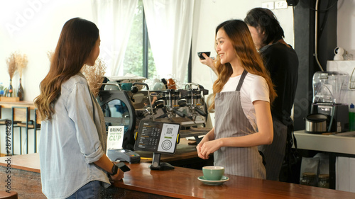 Young asian woman ordering coffee with barista, waitress, small busineaa owner at counter in coffee shop cafe background