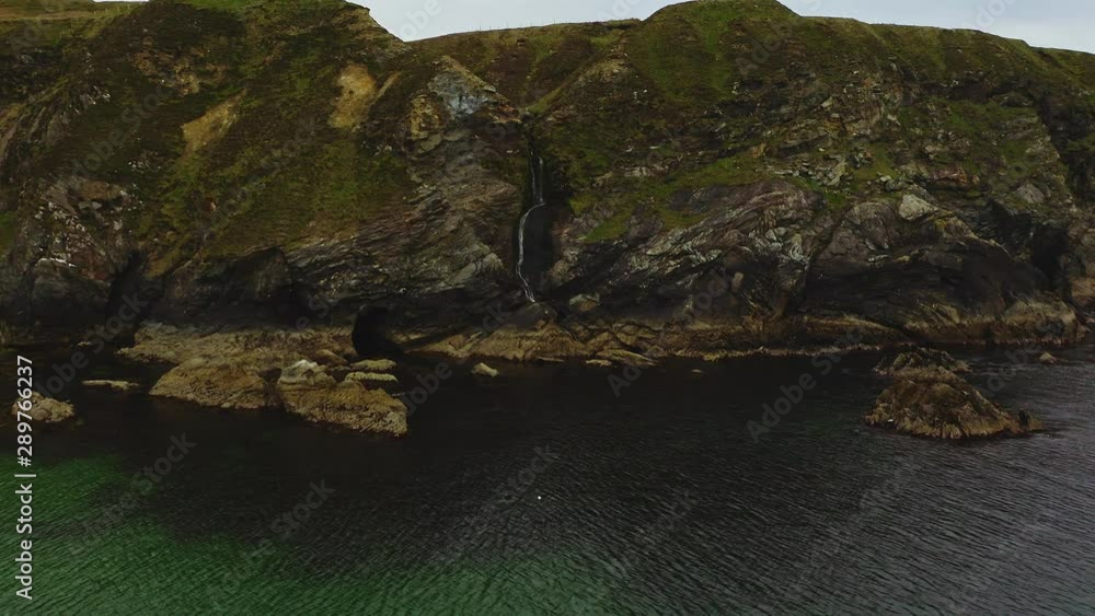 Aerial of small waterfall eroding the side of a cliff in the north of Ireland coastline
