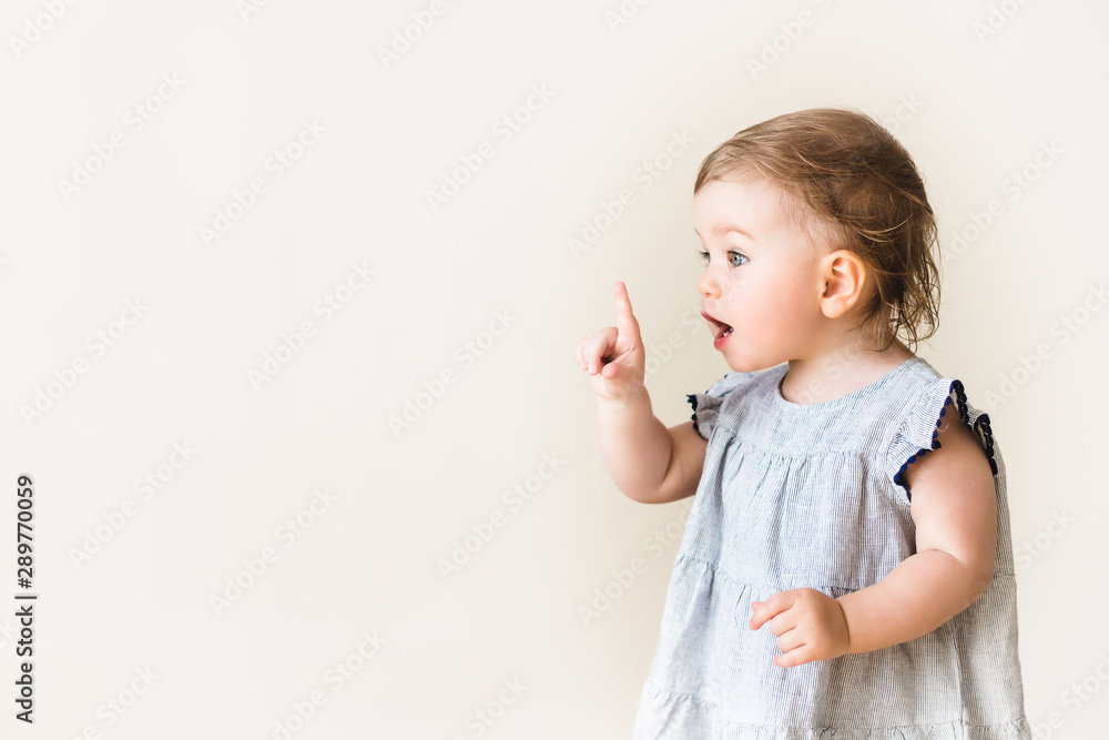 Baby girl pointing her finger, excited and emotional, on neutral background - obrazy, fototapety, plakaty 