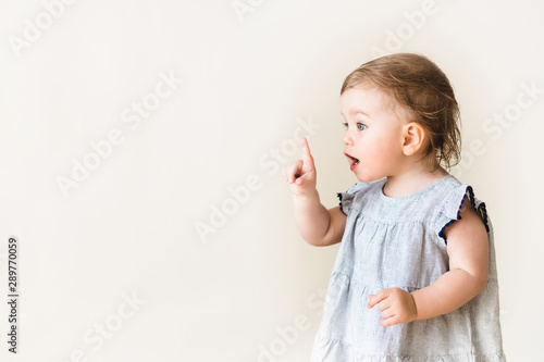 Baby girl pointing her finger, excited and emotional, on neutral background