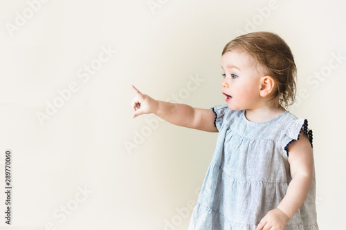 Baby girl pointing her finger, excited and emotional, on neutral background