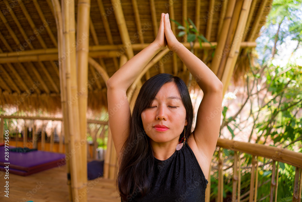 young natural and attractive Asian Chinese woman practicing yoga and meditation exercise outdoors at beautiful wooden joglo studio with tropical jungle view
