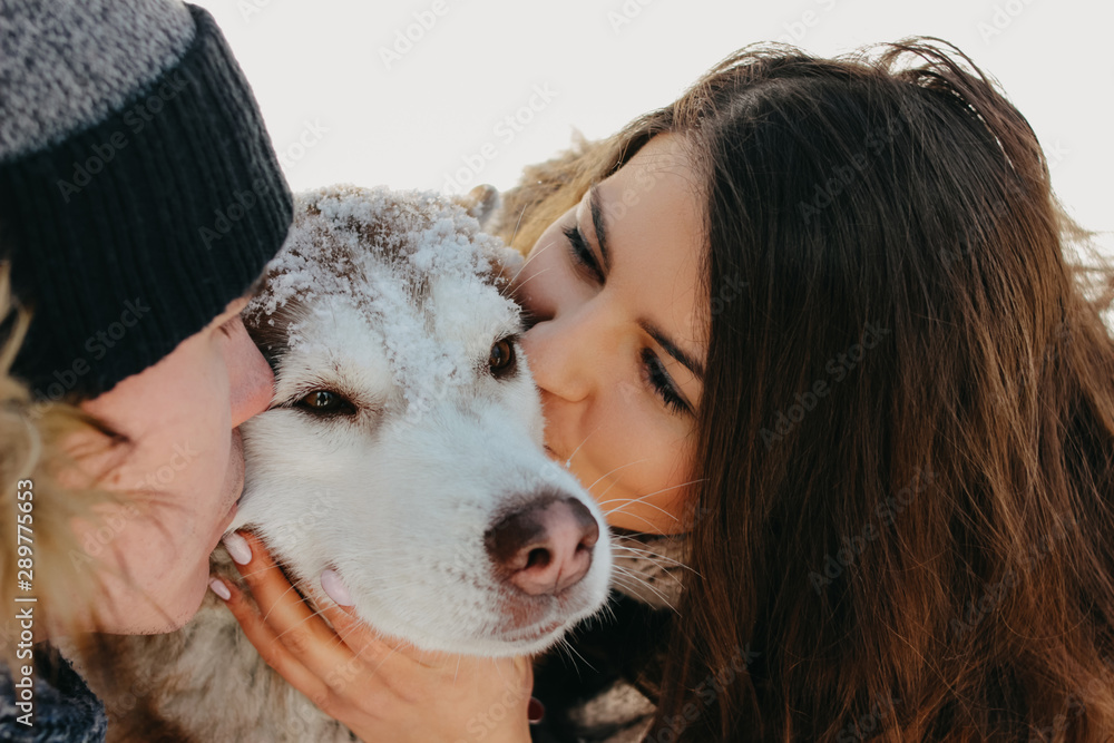 The happy couple kissing dog haski at forest nature park in the cold season. Travel adventure love story The happy couple kissing dog haski at forest nature park in the cold season. Travel adventure love story