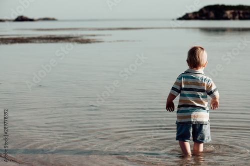 Young toddler walking into beach water, back to camera, copy space