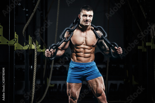 Muscular man bodybuilder training in gym with iron chain and posing. Fit muscle guy workout with weights and barbell