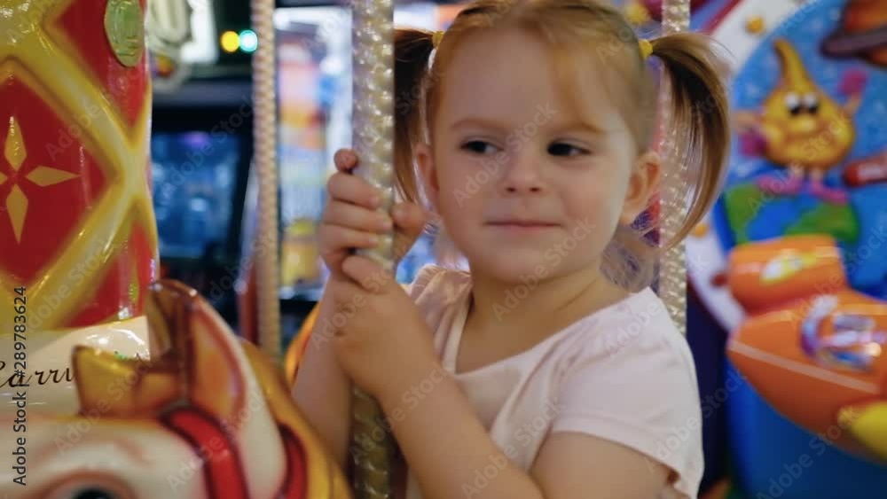 Happy little caucasian girl riding a horse carousel in the game room Happy little caucasian girl riding a horse carousel in the game room