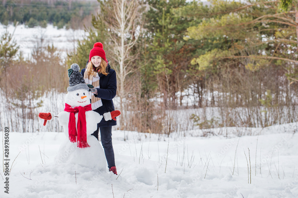 Naklejka premium happy teenager girl with snowman in winter forest