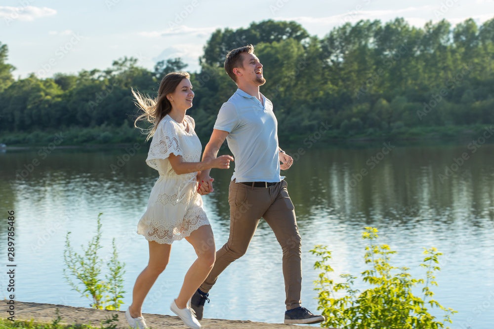 Love and relationship concept - The happy man and woman running in a park near a lake Love and relationship concept - The happy man and woman running in a park near a lake