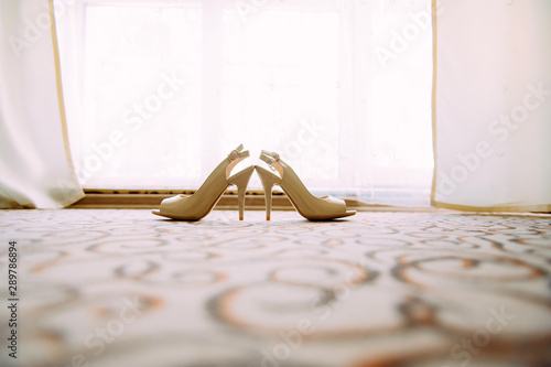 Women's high-heeled shoes on the light carpet in the hotel. Beige wedding shoes on the floor, close-up.