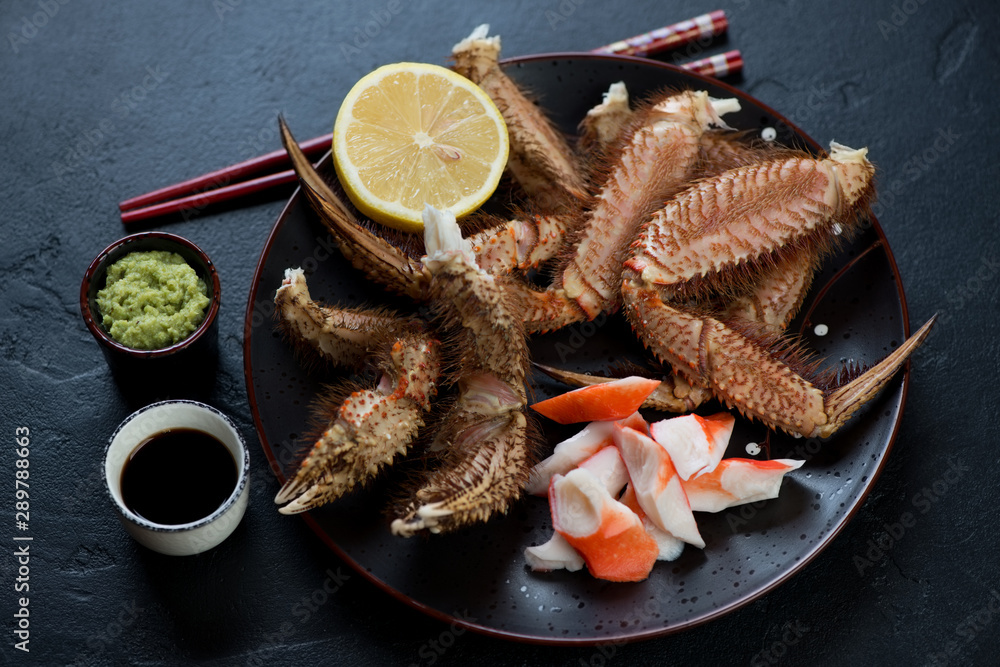 Plate with horsehair crab claws, lemon, wasabi and soy sauce, studio shot over black stone background Plate with horsehair crab claws, lemon, wasabi and soy sauce, studio shot over black stone background