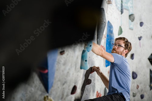 healthy active young sport bearded man in glasses climbing on wall during indoor bouldering training