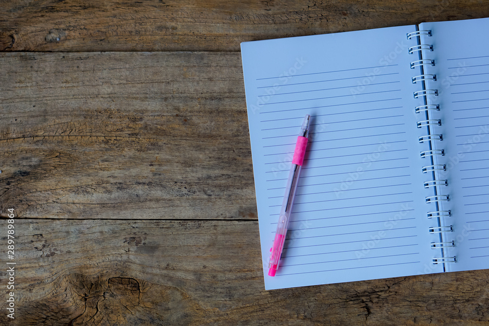 The top view notebook with a pen on a wooden floor with space ideas for inserting text. The top view notebook with a pen on a wooden floor with space ideas for inserting text.
