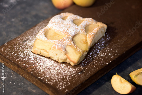 a piece of Apple pie on a wooden Board in powdered sugar on a dark background