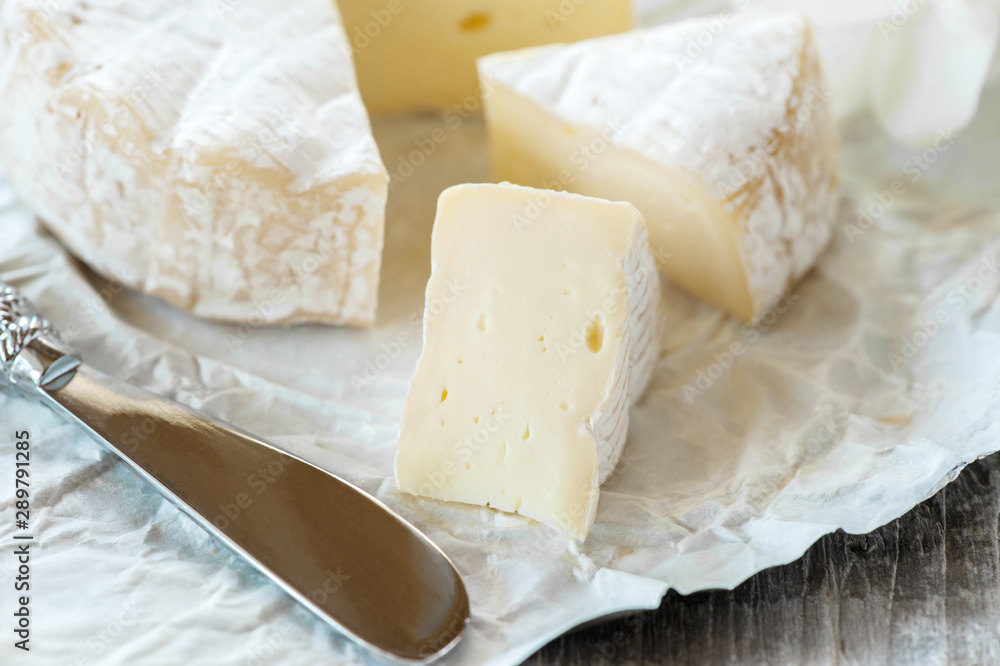 Gourmet spicy Camembert cheese, brie on white paper background with cheese knife. Spicy appetizer for gourmets. Selective focus Gourmet spicy Camembert cheese, brie on white paper background with cheese knife. Spicy appetizer for gourmets. Selective focus