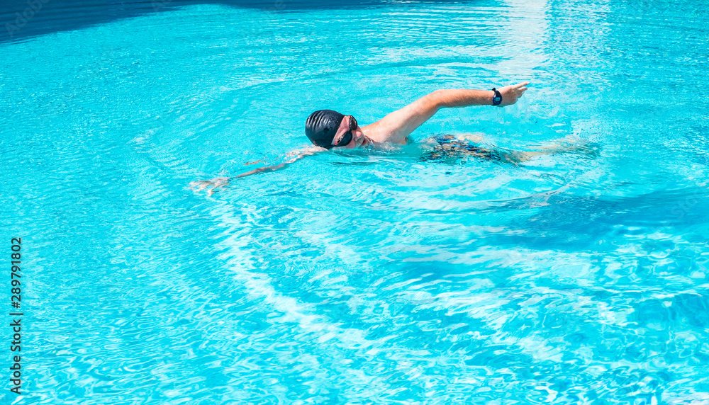 Close-up of a smiling senior people doing sport and swimming in the swimming pool. Black swimming cap and goggles.  Man with white beard and mustache happy with his exercises. Healthy lifestyle.