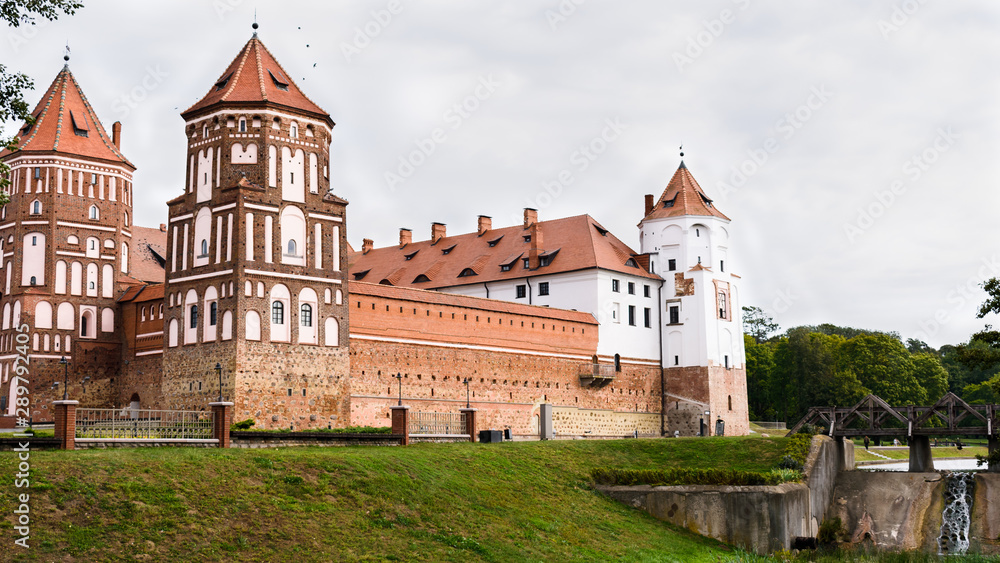 Panorama of the castle in the city of Mir in Belarus. Castle against a cloudy sky with a bridge over a water channel.