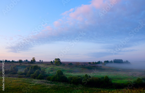 Tranquil hazy landscape with green trees and hills covered by morning fog