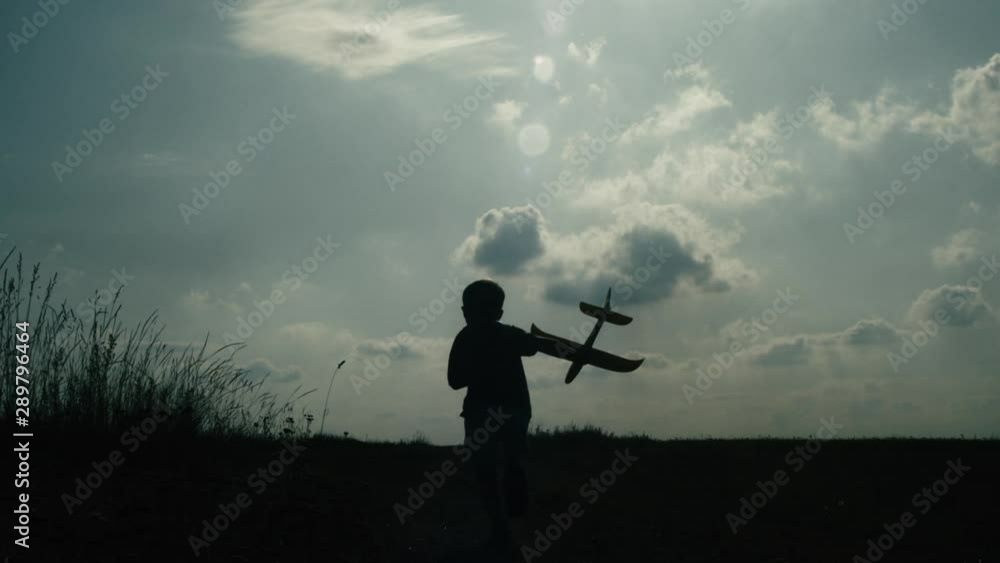 Silhouette of young boy running away from camera with toy airplane raised in his hand. Slow motion. Silhouette of young boy running away from camera with toy airplane raised in his hand. Slow motion.
