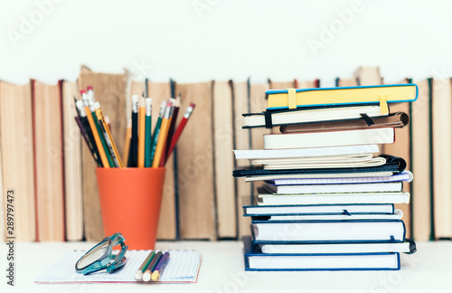 Notebooks piles, stack of books education back to school background, textbooks, glasses and pencils in holder with copy space for text.