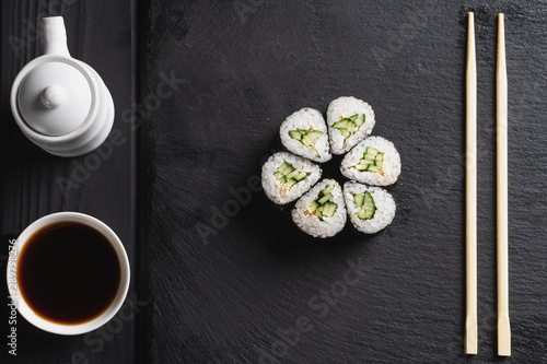 Sushi Set nigiri and sushi rolls in dark stone plate with soy sauce and chopsticks over black background.