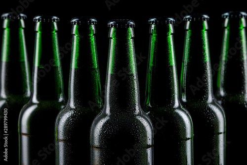 Row of wet glass bottles of beer on dark background