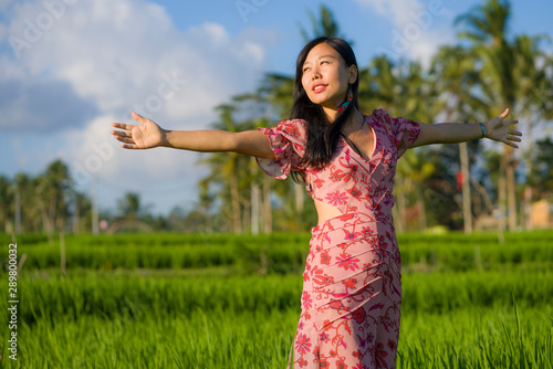 natural and fresh lifestyle portrait of young beautiful and attractive Asian Chinese woman in elegant dress walking on green rice field enjoying exotic Summer holidays