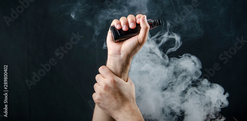 hand holding vape e-cigarette or electronic cigarette with white smoke over a black background. 