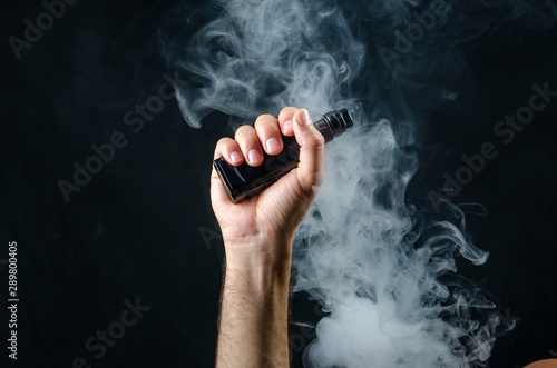 hand holding vape e-cigarette or electronic cigarette with white smoke over a black background. 