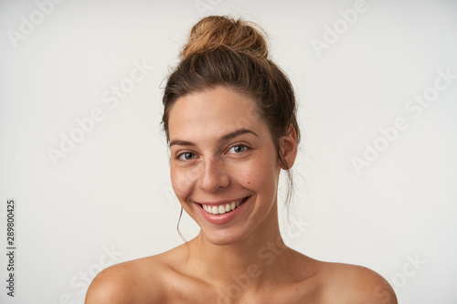 Indoor portrait of joyful young female smiling sincerely to camera  looking beautiful without make-up  standing over white background