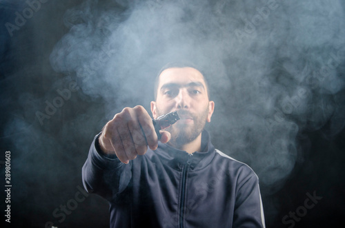 vape and smoke vape electronic e-cigarette or e-cig by a young man with smoke clouds over a black background. © Hazem