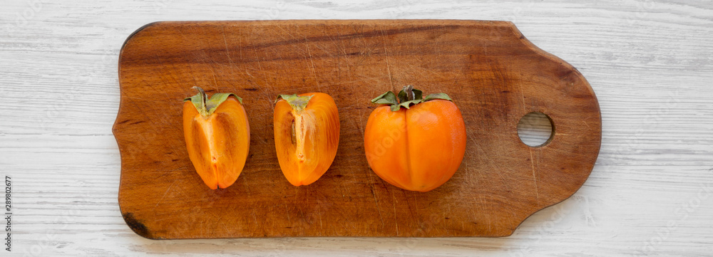 Fresh persimmon on a chopping board on white wooden background, top view. Flat lay, overhead, from above. Close-up. Fresh persimmon on a chopping board on white wooden background, top view. Flat lay, overhead, from above. Close-up.