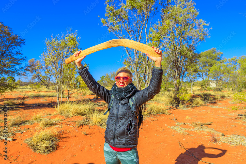 Foto Stock Happy tourist woman holding an aboriginal weapon of boomerang  used by Luritja and Pertame people in Central Australia, Northern  Territory. Red sand in desert outback. Bush wilderness in dry season.
