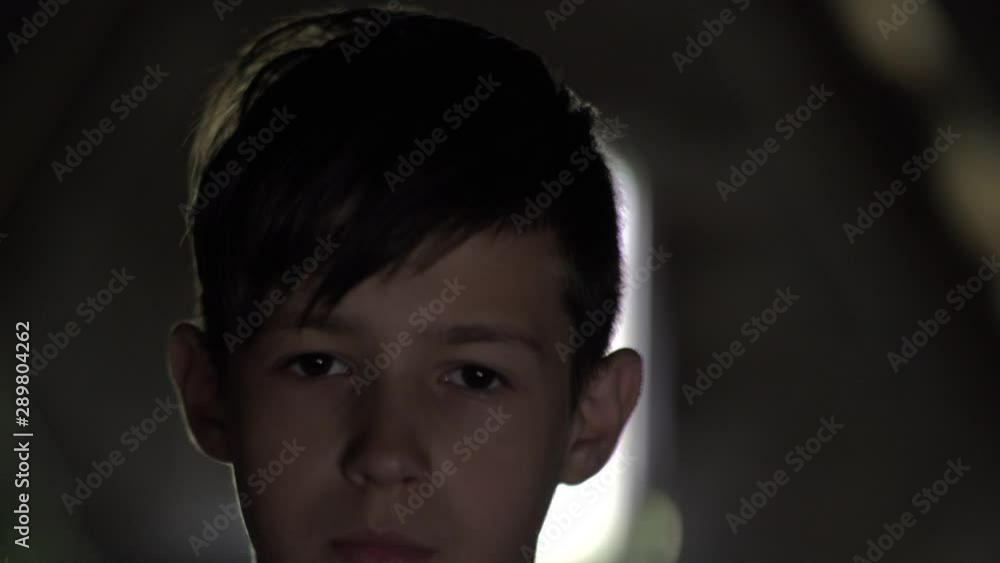 portrait of a serious sad boy in a dark room, pain on face, look at the camera portrait of a serious sad boy in a dark room, pain on face, look at the camera