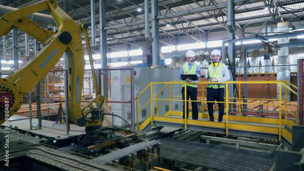 Factory workers are managing modern robotic arm working