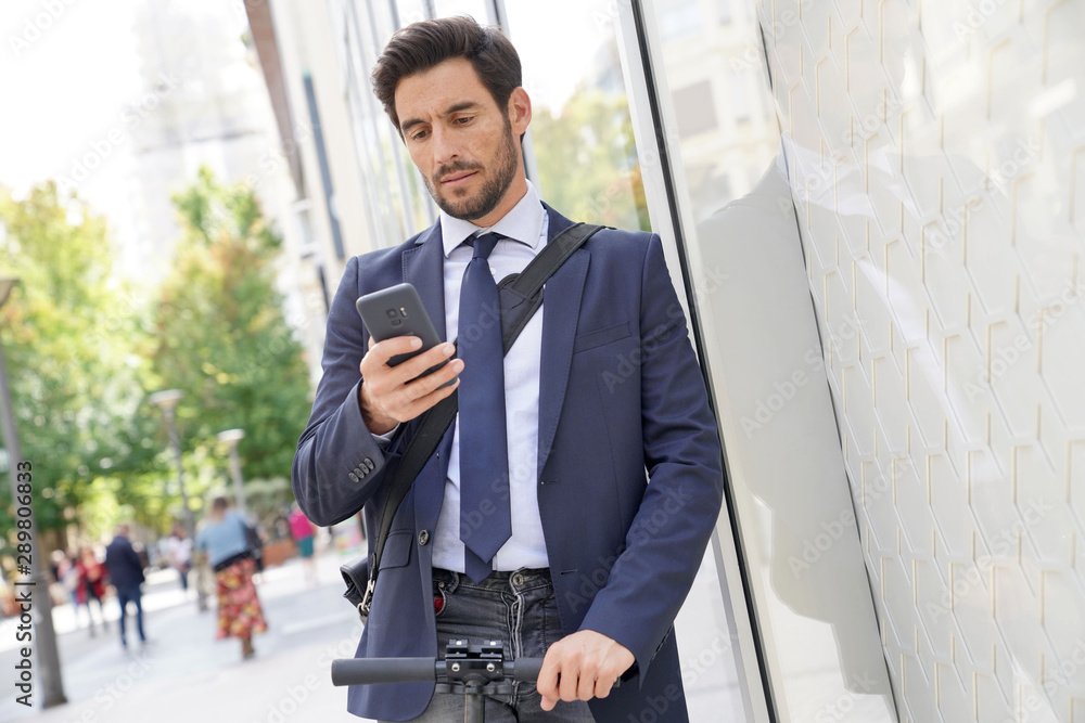 Businessman in the street using smartphone and electric scooter Businessman in the street using smartphone and electric scooter